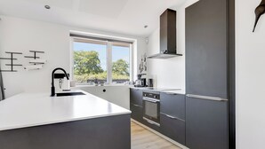 A modern kitchen with a large island, dark cabinetry, and a window with a view of trees. - New and modern holiday home with hot tub (Frørup)