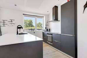 A modern kitchen with a large island, dark cabinetry, and a window with a view of trees.