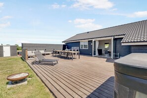 En overdækket terrasse med grill, liggestole og et bord.
