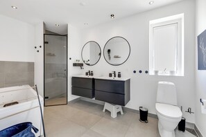 A modern bathroom with a glass shower, two round mirrors, a white toilet, and a white sink with a black countertop.
