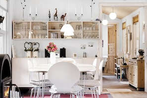 A modern kitchen with white cabinetry, a dining area with a white table and chairs, and a hallway with wooden doors.