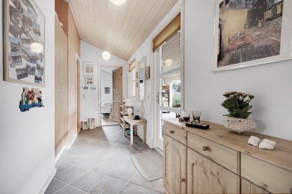 A hallway with a wooden ceiling, tiled floor, and a wooden cabinet with a vase and a plant.
