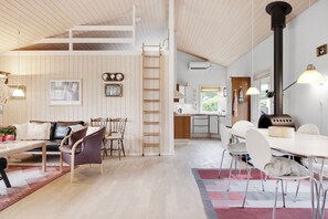 A spacious living area with a high ceiling, a dining table, chairs, a sofa, a fireplace, and a kitchen in the background.