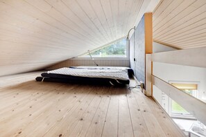 Ein kleines Schlafzimmer im Dachgeschoss mit schrägen Wänden, einem Einzelbett und einem Fenster mit Blick nach draußen.
