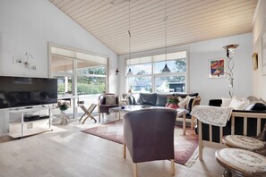 Ein geräumiges Wohnzimmer mit großem Flachbildfernseher, bequemen Sitzgelegenheiten und Blick ins Freie.