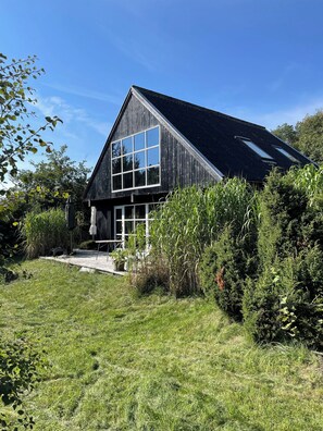 A modern house with a sloped roof, large windows, and a well-maintained lawn.