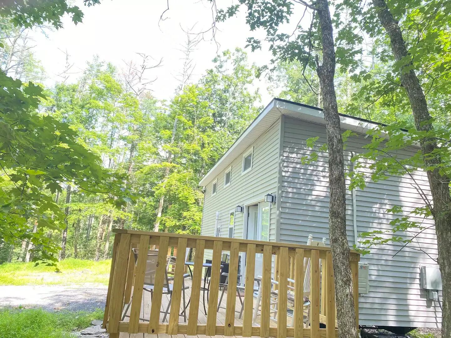 A wooden deck with outdoor furniture, a small house with a gabled roof, and surrounding trees.