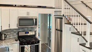 A modern kitchen with white cabinets, a stainless steel refrigerator, a microwave, and a gas stove.