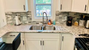 A kitchen with white cabinets, a granite countertop, a stainless steel sink, and a window with a view of trees.