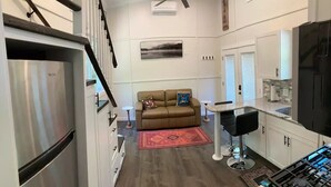 A compact kitchen with a stainless steel refrigerator, a bar stool, and a dining area with a red rug.