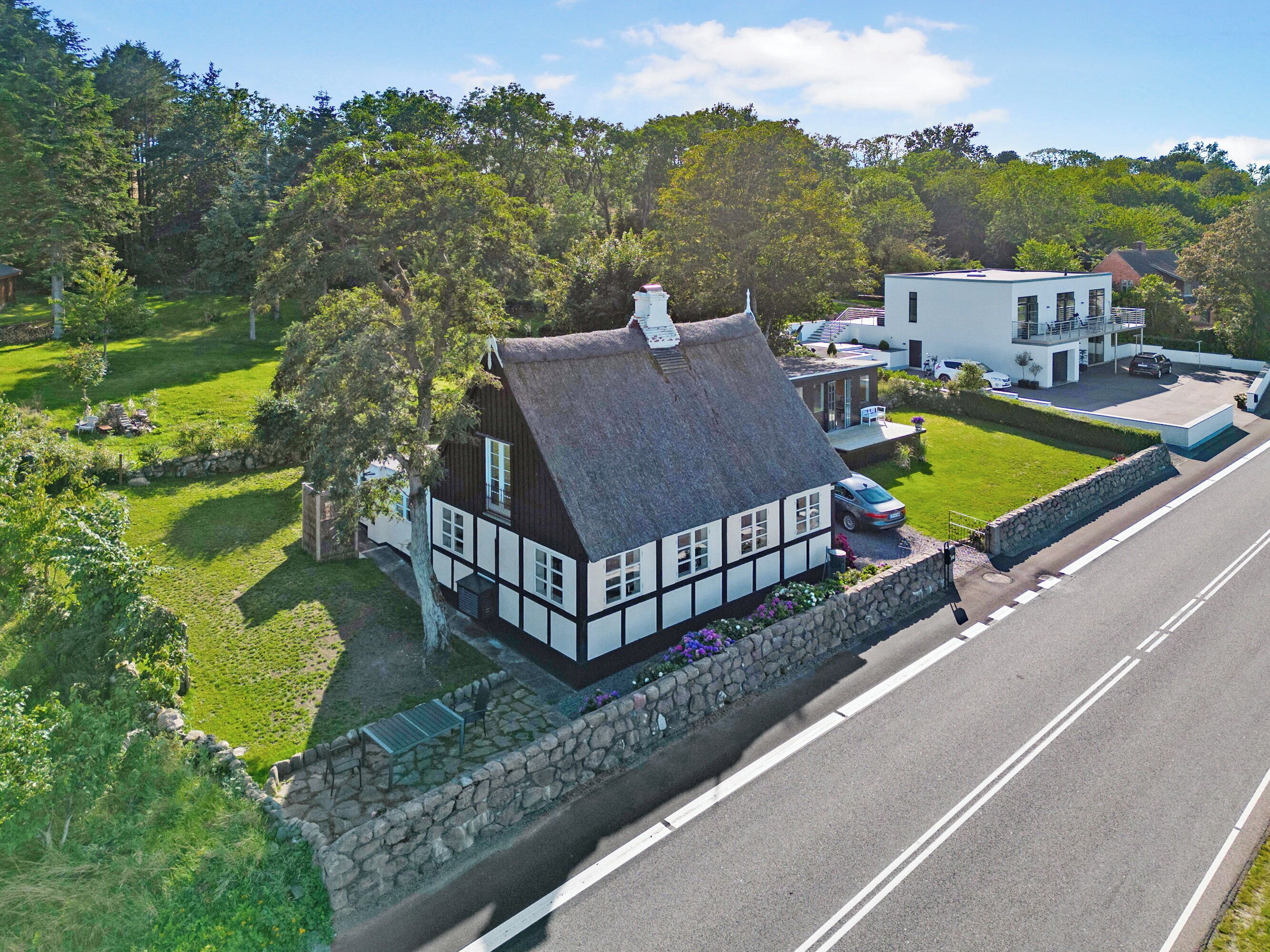 A traditional half-timbered house with a thatched roof, a stone wall, and a well-maintained lawn.