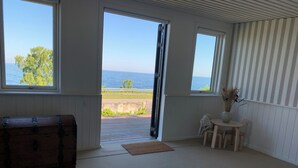 Et værelse med et stort vindue, en træskrin, et lille bord med en vase og et mønstret tæppe.