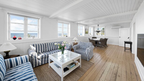 En rummelig stue med stribede sofaer, et glasbord og store vinduer.