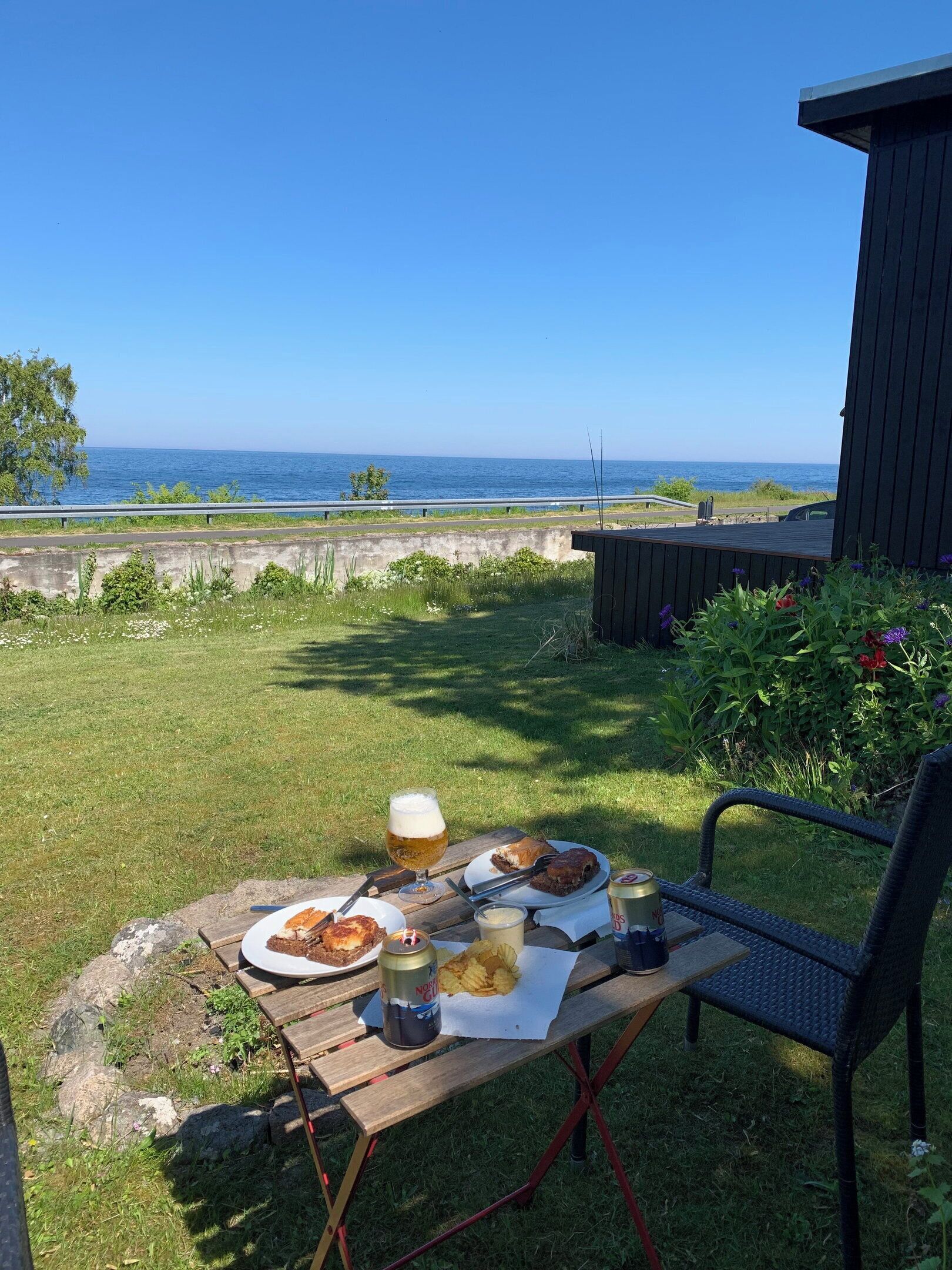 Et picnicbord med mad og drikke, en stol og udsigt til havet.