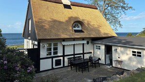 Et traditionelt hus med stråtækt tag, en stenspir og havudsigt.