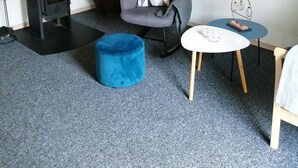 A cozy room with a black wood stove, a blue ottoman, a grey armchair with a patterned cushion, and a small white table with decorative items. - Summer house for relaxation and activity (Gråsten)