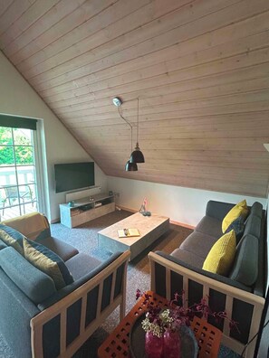 A cozy loft-style living room with a sloped ceiling, a flat-screen TV, a coffee table, and two sofas with cushions. - Summer house for relaxation and activity (Gråsten)