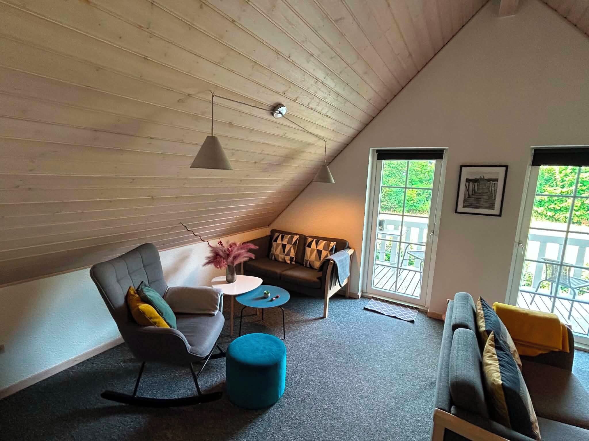 Une pièce confortable de style loft, avec un plafond en pente, un canapé, un fauteuil, une petite table ronde et un pouf bleu.