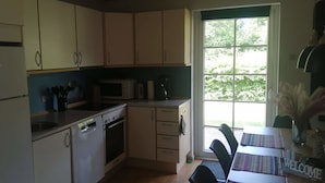 A compact kitchen with a refrigerator, microwave, stove, and sink. There is a window with a view of greenery outside. - Summer house for relaxation and activity (Gråsten)