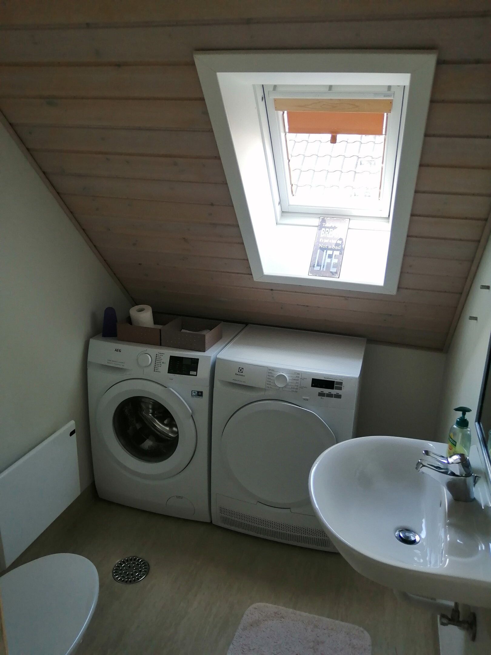 A compact room with two washing machines, a sink, a toilet, and a skylight.