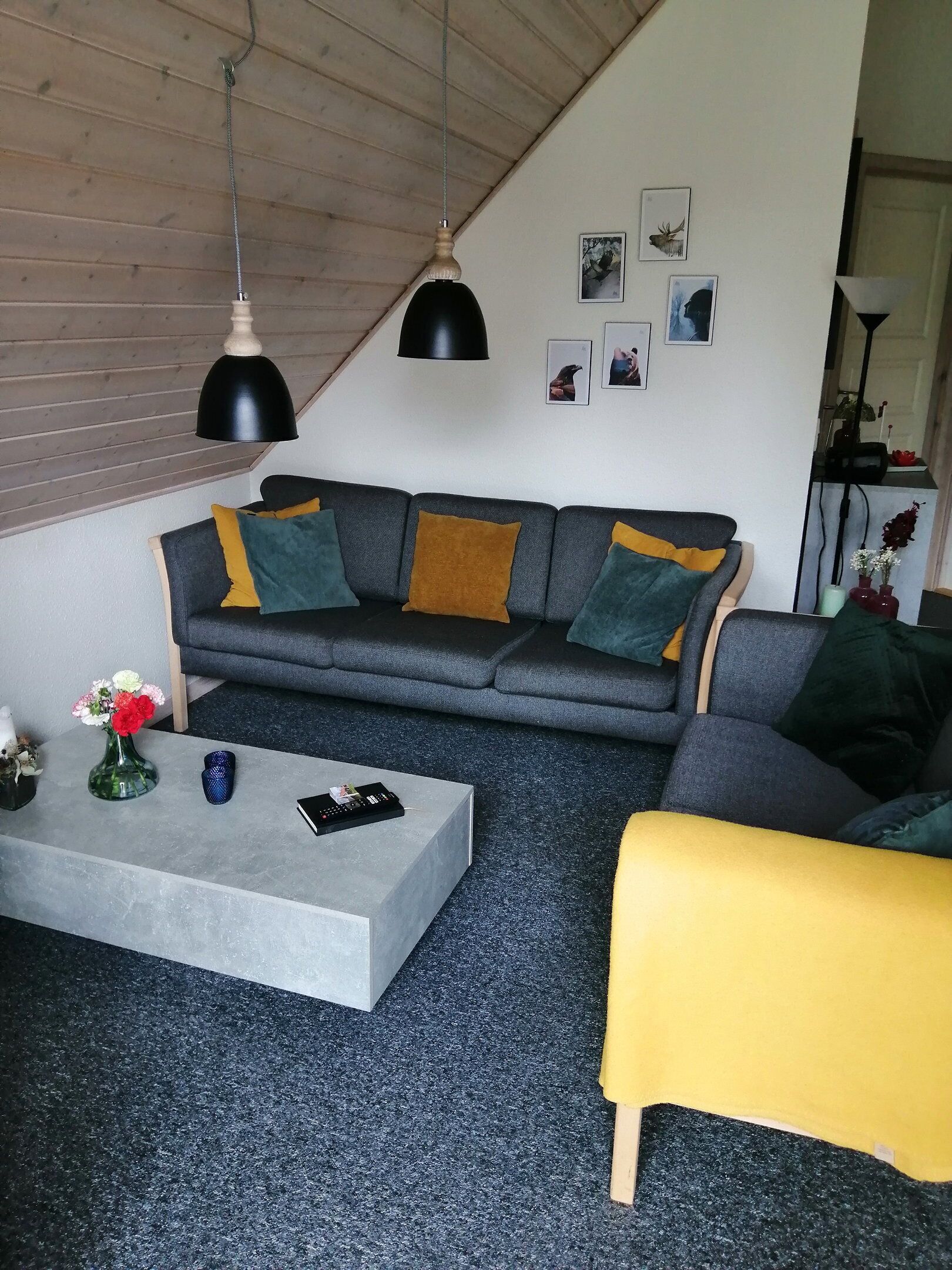 Ein modernes Wohnzimmer mit einem grauen Sofa, einem gelben Hocker und einem Couchtisch mit Vase und Fernbedienung.