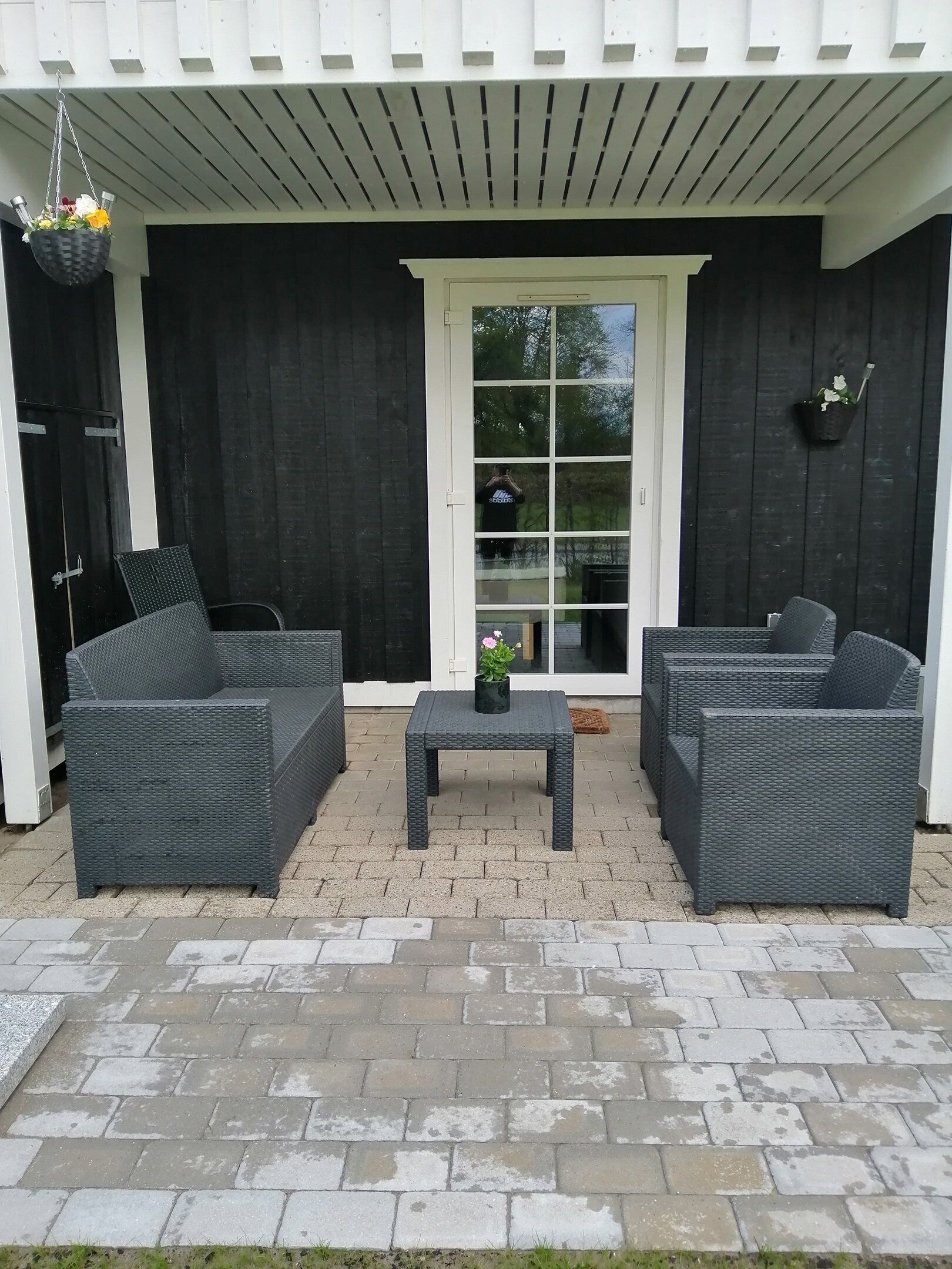 Een terras met twee rieten banken, een kleine tafel en hangmanden met bloemen.