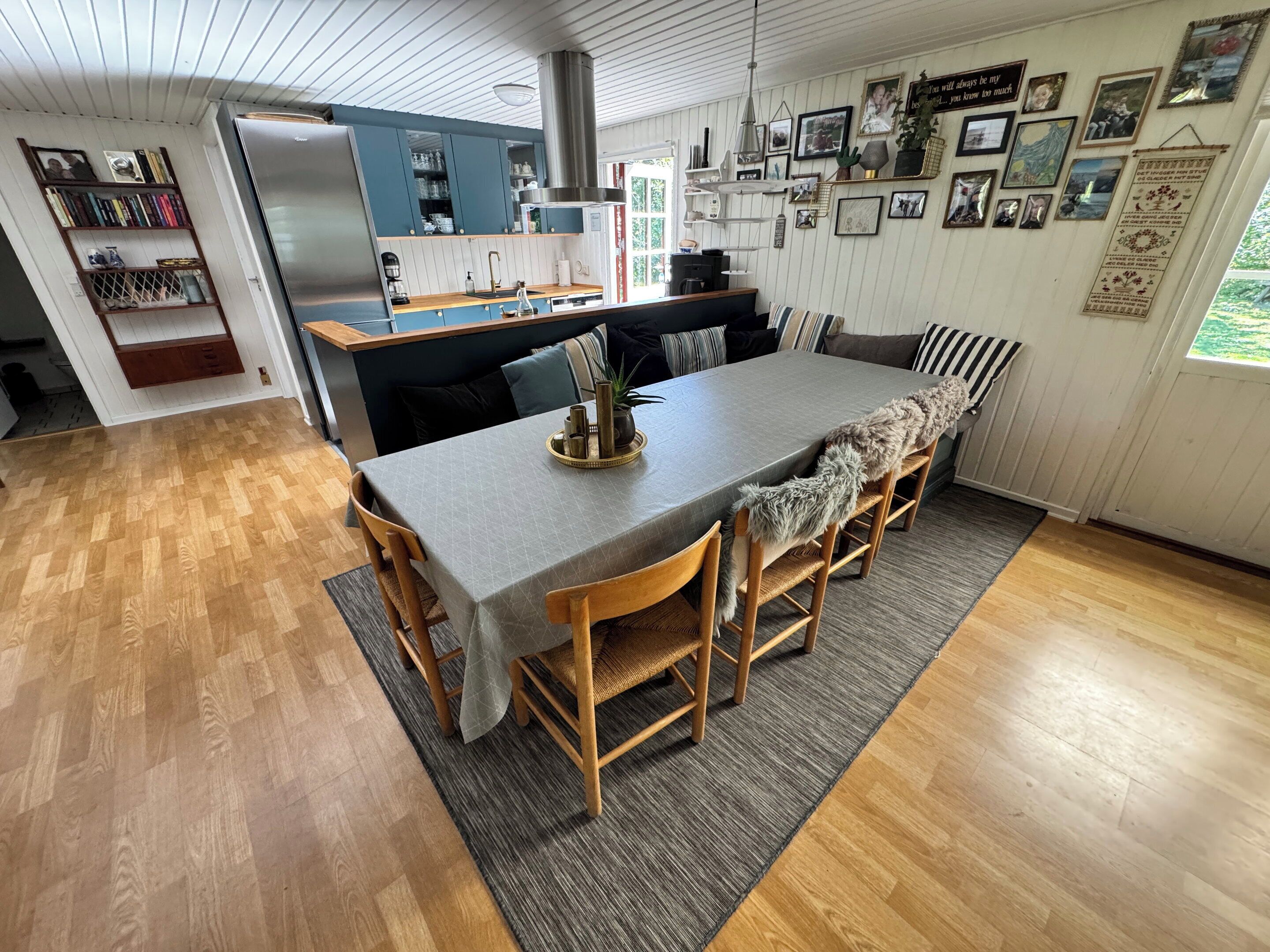 A dining area with a table, chairs, a rug, and a kitchen in the background.