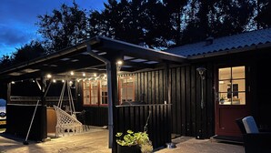 Ein überdachter Außenbereich mit Grill, Sitzgelegenheit und Blumentöpfen.