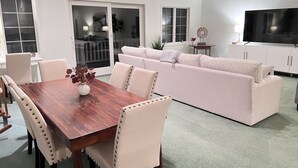 Un salon moderne avec une table à manger en bois, un canapé beige et un téléviseur à écran plat.