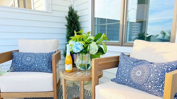 Une terrasse avec deux chaises en bois, une petite table ronde, une bouteille de champagne et un vase rempli de fleurs.