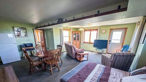 A compact room with a bed, a dining table with chairs, a sofa, a television, and a refrigerator.