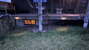 A rustic wooden deck with a tree stump and a wheel, surrounded by a grassy area.