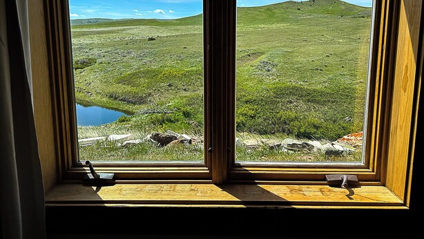A window with a view of a grassy landscape, a small body of water, and distant hills.