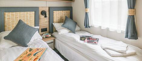 A hotel room with two beds, a nightstand, a clock, and a window with curtains.