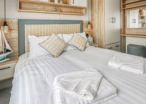 A neatly made bed with striped bedding, multiple pillows, and folded towels. - Large 12ft-wide caravan with one double with en suite W. (Cardigan)