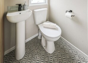 A bathroom with a toilet, sink, and patterned floor tiles. - Large 12ft-wide caravan with one double with en suite W. (Cardigan)