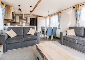 A modern RV interior with two grey sofas, a wooden table, a dining area, and a kitchen.