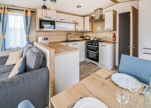A compact kitchen with a microwave, stove, and sink. There is a dining area with a table set for two, and a sofa with cushions.