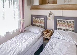 A bedroom with two single beds, a wooden headboard, a bedside table with a basket, and a window with curtains.