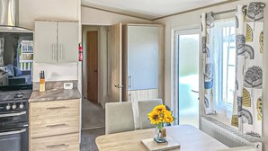 A compact kitchen with modern appliances, a dining area with a table and chairs, and a large window with patterned curtains.