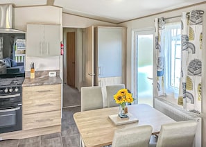 A compact kitchen with modern appliances, a dining area with a table and chairs, and a large window with patterned curtains. - This stunning holiday home with a double bedroom and en suite W. (Bishop Auckland)