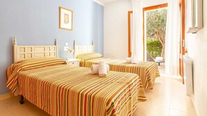 A hotel room with two beds, a ceiling fan, a framed picture on the wall, and a view of greenery outside. - Nice apartment near the beach in Port de Pollença (Port de Pollença)
