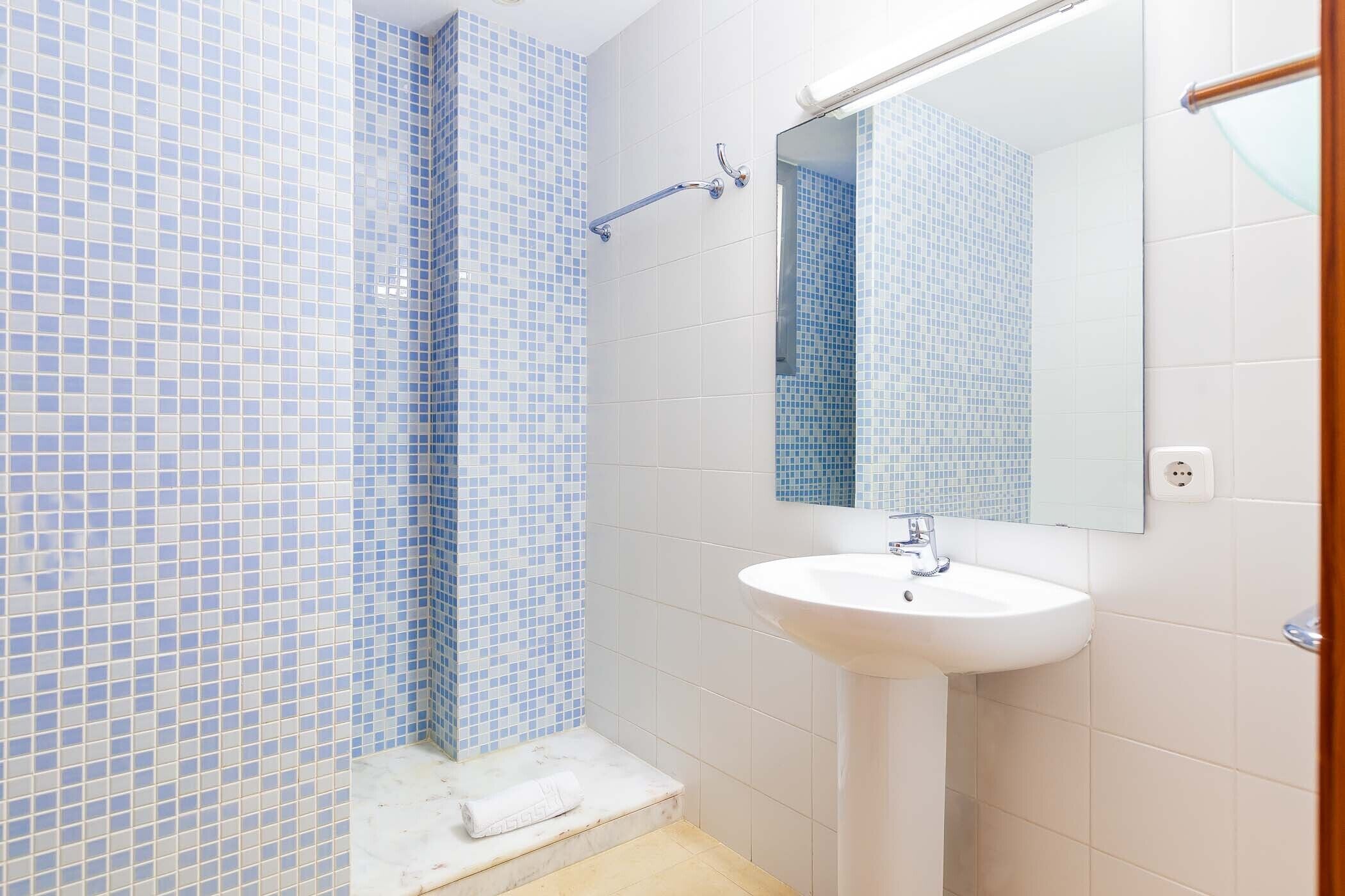 A bathroom with a white sink, a mirror, and blue-tiled walls.