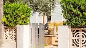 A gated entrance with a metal gate and decorative panels, flanked by trimmed hedges and a potted plant. - Nice apartment near the beach in Port de Pollença (Port de Pollença)