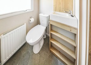 A modern bathroom with a toilet, a white sink, and a wooden shelf unit. - Large 12ft-wide caravan with one double with en suite W. (Cardigan)