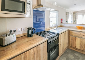Una kitchenette equipada con microondas, tostadora, hervidor, estufa, pileta y alacenas de madera.