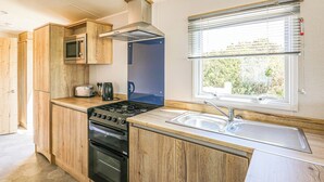 A compact kitchen with wooden cabinets, a built-in microwave, a stove, and a window with blinds.