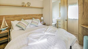 A neatly made bed with white linens, a wooden headboard, and a small shelf with decorative items.