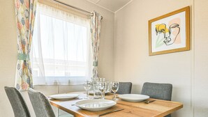 A dining area with a wooden table, four grey chairs, and a window with patterned curtains.