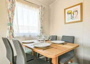A dining area with a wooden table, four grey chairs, and a window with patterned curtains. - Large 12ft-wide caravan with one double with en suite W. (Cardigan)